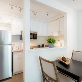 A modern apartment kitchen with white cabinets and a dining area featuring stainless steel appliances.