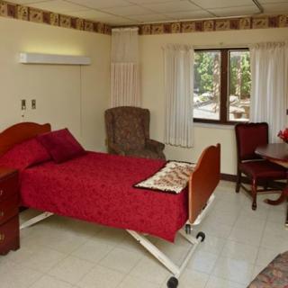 A cozy bedroom with a hospital bed, recliner chair, and window with curtains.