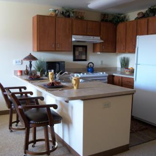 A modern kitchen with wooden cabinets, a large white refrigerator, and a countertop with bar stools.