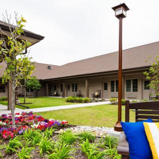 A tranquil courtyard featuring a vibrant garden with blooming flowers, a wooden bench, and a classic lamp post beside a building.