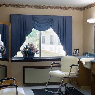 A cozy beauty salon interior with a styling chair, mirror, and window adorned with blue curtains.