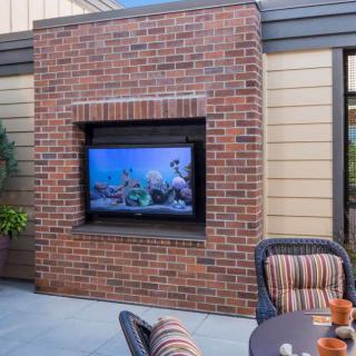 A cozy outdoor patio featuring a brick wall with a mounted TV and comfortable seating.
