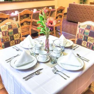 A neatly set dining table in a restaurant with a white tablecloth and elegant place settings.