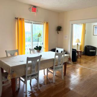 A bright dining area with a wooden table and chairs, featuring large windows with yellow curtains.