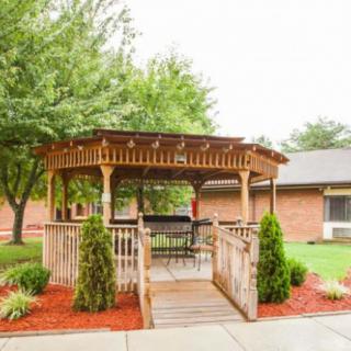 A wooden gazebo surrounded by landscaped gardens and a concrete pathway.