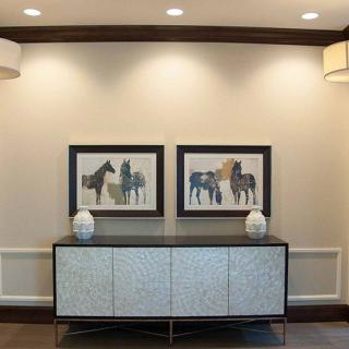 A modern interior featuring a console table adorned with two vases and framed artwork of horses on the wall.