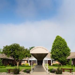 A welcoming entrance to a modern building surrounded by greenery under a clear sky.