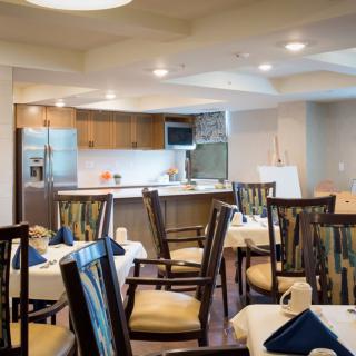 A modern dining room with neatly arranged tables and chairs, adjacent to a stylish kitchen.