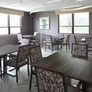 An empty dining area with multiple tables and chairs, well-lit by natural light from the windows.
