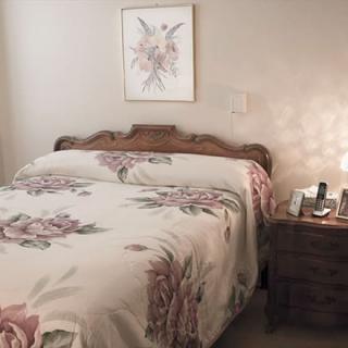 A cozy bedroom features a floral-patterned bedspread and classic wooden furniture, accompanied by a softly lit lamp on the nightstand.
