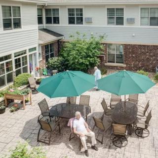 A peaceful outdoor patio area with tables, green umbrellas, and seating in a senior living community.