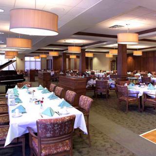 An elegant dining room with neatly arranged tables and a grand piano in the corner.