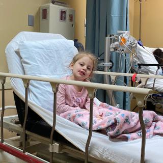 A young child resting on a hospital bed, displaying a brave smile in a medical setting.