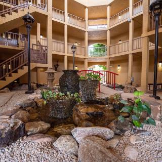 An indoor atrium with a central water feature surrounded by rocks and greenery, enclosed within a multi-story building.