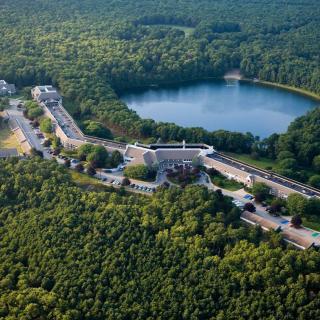 An aerial view of a lush forest area with a lake, surrounding roads, and buildings.