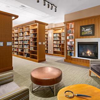 A cozy library space featuring wooden bookshelves, a fireplace, and comfortable seating.