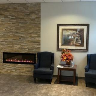 A cozy waiting room with comfortable chairs, a modern fireplace, and decorative artwork on the wall.