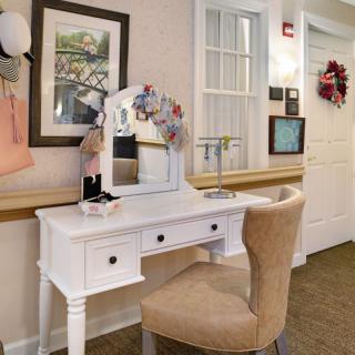 A stylish vanity setup with a mirror and flowers, complemented by a cozy chair in a warmly decorated room.