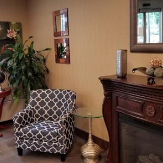 A cozy living room corner featuring a patterned armchair beside a fireplace, adorned with decorative pieces and greenery.