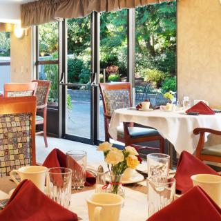 A cozy restaurant dining area with elegantly set tables and a view of the garden through glass doors.