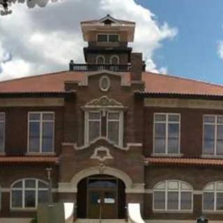 A historic brick building with a prominent tower and large windows under a cloudy sky.