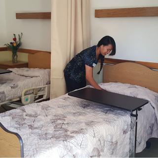 A healthcare staff member making a bed in a patient room.