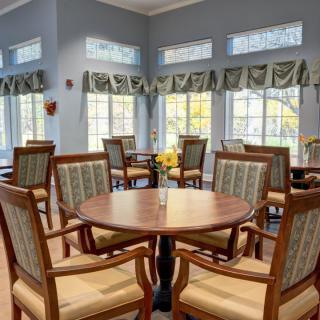 A well-lit dining area with round tables and cushioned chairs near large windows.