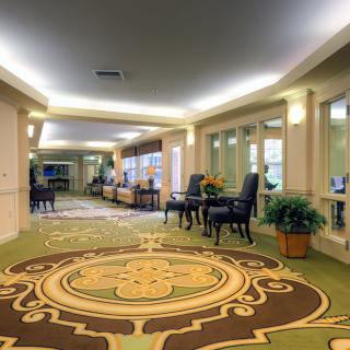 A spacious and elegantly decorated hallway with patterned carpets, comfortable seating areas, and indoor plants.