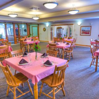 A cozy dining room with pink tablecloths and neatly arranged wooden chairs.