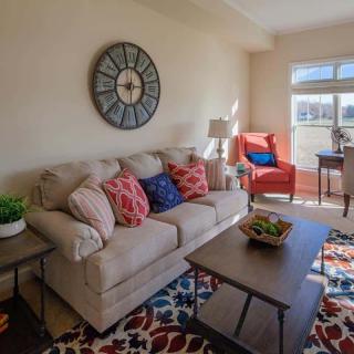A cozy living room with a beige sofa, vibrant cushions, and a large wall clock.