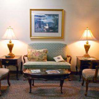 A cozy living room setup with a sofa, chairs, lamps, and a coffee table beneath a framed painting.