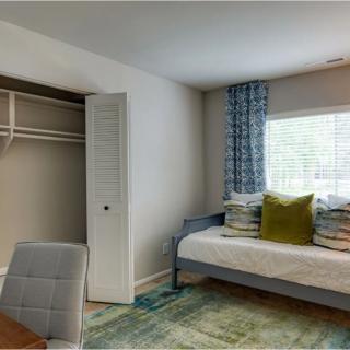 A cozy bedroom featuring a bed with decorative pillows, a closet, and a desk by the window.
