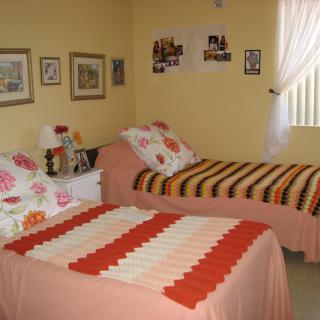 A cozy bedroom with two twin beds adorned with crochet blankets and decorative pillows, complemented by wall art and sheer curtains.