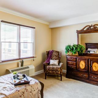 A cozy bedroom featuring a window, elegant dresser, and comfortable armchair.