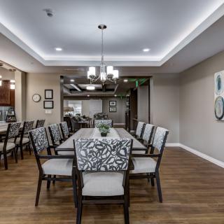 A modern dining room with a long table surrounded by upholstered chairs and elegant lighting.