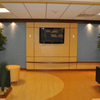 A modern waiting room with comfortable seating, a television, and decorative plants.