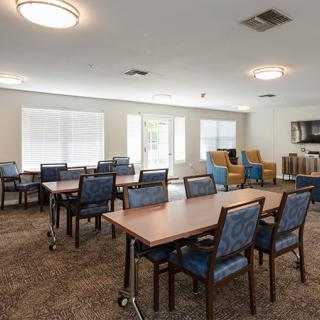 A community dining area with tables and chairs, featuring large windows for natural light.