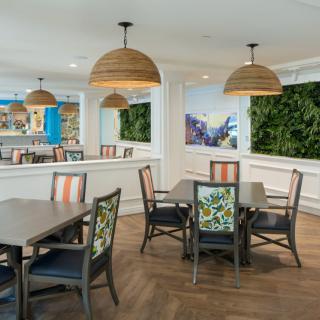 A modern dining area featuring wooden tables and chairs, pendant lighting, and vibrant plant decor.