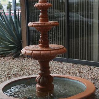 A decorative three-tiered terracotta fountain surrounded by gravel.