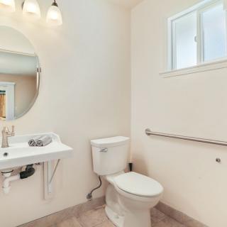A modern, minimalist bathroom featuring a toilet, sink, mirror, and handrail next to a small window.