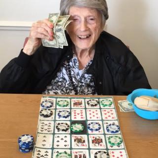 An elderly woman happily holding cash while playing a bingo game.