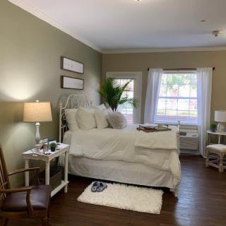 A cozy bedroom with a neatly made bed, soft lighting, and a large window letting in natural light.