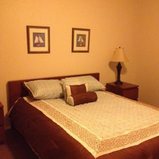A cozy bedroom with a neatly made bed, framed artwork on the wall, and two nightstands with a lamp.