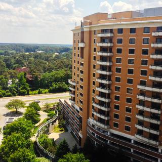 A tall apartment building surrounded by greenery and a winding road.
