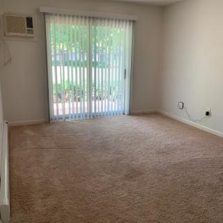 An empty room with carpet flooring, a sliding glass door with vertical blinds, and an air conditioner.