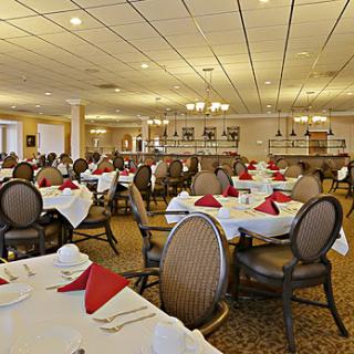 An elegant dining room set up for a meal, featuring neatly arranged tables with white tablecloths and red napkins.