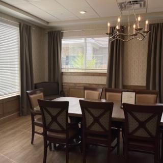 A well-lit dining room with a large table, elegant chairs, and a chandelier.