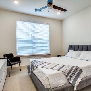 A modern, minimalist bedroom with a comfortable bed, stylish chair, and a ceiling fan for a cozy atmosphere.