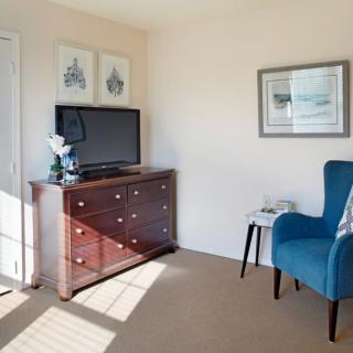 A cozy living room corner featuring a wooden dresser with a television on top, a blue armchair, and framed artwork on the walls.