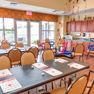 A community event room with tables and chairs set up, featuring a small kitchen area in the background.